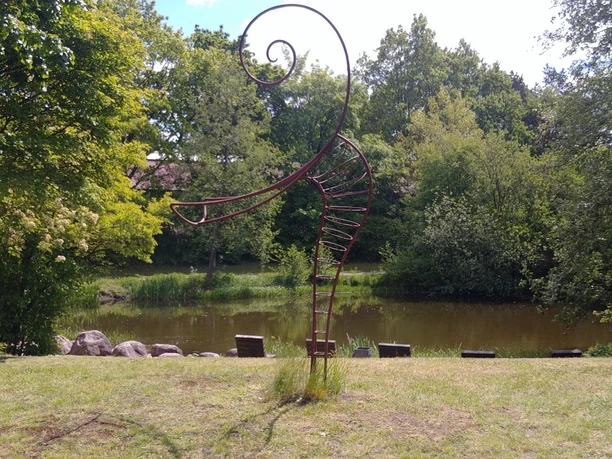 Füllhorn oder Figura Eine spiralige Metallskulptur steht vor einem Teich in einem parkähnlichen Bereich, umgeben von Bäumen.