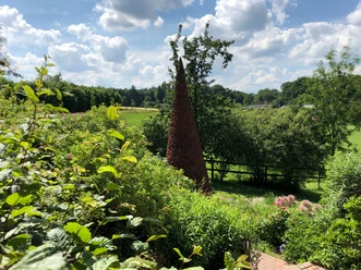 Ein markanter, spitzer Ziegelturm erhebt sich inmitten einer grünen und bewachsenen Landschaft.