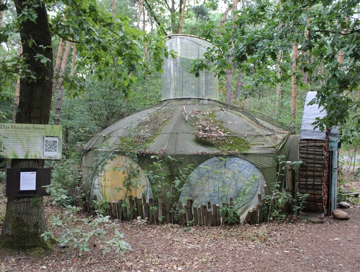 Skulptur Haus der Sonne Eine runde Skulptur aus Holz und Draht im Wald von Nartum, Niedersachsen, von Pflanzen umgeben.
