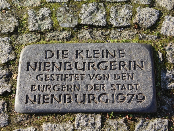 Gedenktafel „Kleine Nienburgerin“ aus dem Jahr 1979, umgeben von Kopfsteinpflaster.