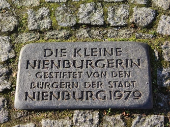 Schild Kleine Nienburgerin Gedenktafel „Kleine Nienburgerin“ aus dem Jahr 1979, umgeben von Kopfsteinpflaster.