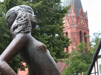 Kleine Nienburgerin Bronzestatue eines Mädchens vor der St. Martin Kirche in Nienburg mit erhobenem Blick und Bäumen.
