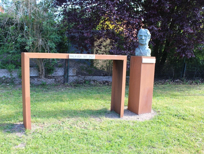 Bronzene Büste von Gottlieb Pot d'Or auf Steinsockel, verbunden durch moderne Stahlkonstruktion im Grünen.