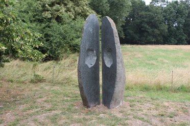 Skulptur "Geöffnete Form" Skulptur aus Stein mit zwei stehend getrennten Halbschalen vor grünem Waldhintergrund.