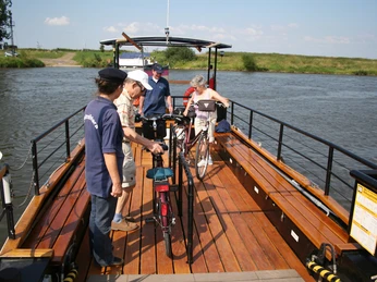 PetraSolara mit Radfahrern Eine kleine Fahrzeugfähre überquert einen Fluss mit Radfahrern an Bord an einem sonnigen Tag.