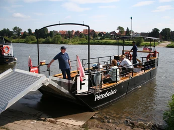 Anlegestelle PetraSolara Fähre PetraSolara überquert Fluss mit Passagieren, umgeben von grüner Landschaft und Dörfern.