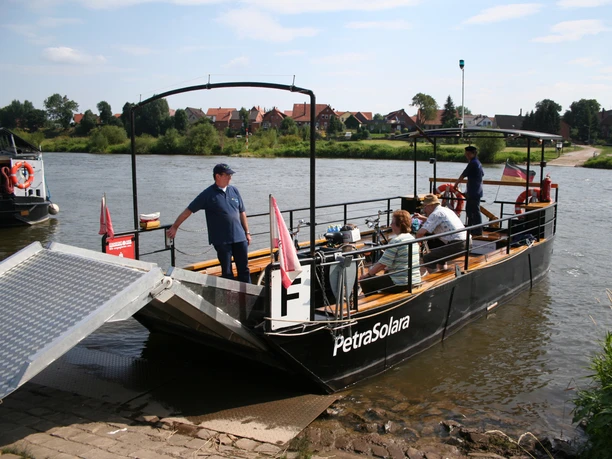Anlegestelle PetraSolara Fähre PetraSolara überquert Fluss mit Passagieren, umgeben von grüner Landschaft und Dörfern.