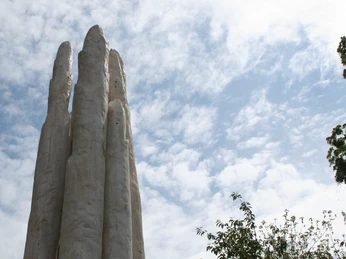 Spargelskulptur Weiße Spargelskulptur erhebt sich vor einem bewölkten blauen Himmel, umgeben von Bäumen.