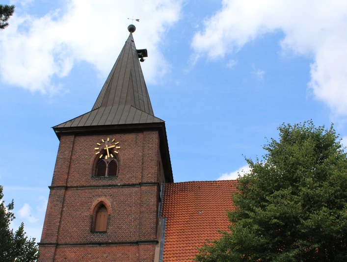 Backsteinkirche mit markantem Kirchturm und Uhr in grüner Umgebung unter blauem Himmel.