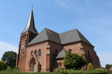Kirche Lunsen Historische Backsteinkirche mit hohem Turm und Spitzdach vor klarem blauen Himmel und grüner Vegetation.