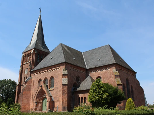 Kirche Lunsen Historische Backsteinkirche mit hohem Turm und Spitzdach vor klarem blauen Himmel und grüner Vegetation.