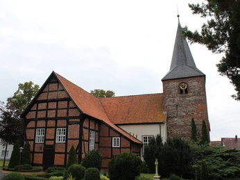 St. Georgs-Kirche Warmsen Ehemalige Wehrkirche in Warmsen mit markantem Fachwerk und hohen Bäumen im Vordergrund.