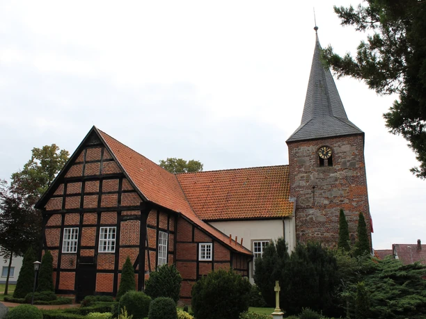 St. Georgs-Kirche Warmsen Ehemalige Wehrkirche in Warmsen mit markantem Fachwerk und hohen Bäumen im Vordergrund.
