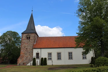 St. Georgs-Kirche Warmsen Backsteinkirche im Grünen, aufgenommen unter blauem Himmel, mit markantem Glockenturm und Ziegeldach.