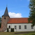 St. Georgs-Kirche Warmsen Backsteinkirche im Grünen, aufgenommen unter blauem Himmel, mit markantem Glockenturm und Ziegeldach.
