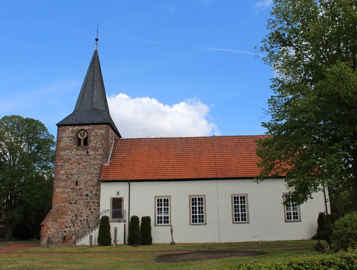 St. Georgs-Kirche Warmsen Backsteinkirche im Grünen, aufgenommen unter blauem Himmel, mit markantem Glockenturm und Ziegeldach.
