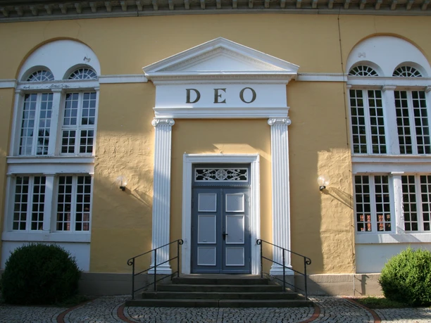St.-Jacobi-Kirche Stolzenau Gelbe Kirchenfassade mit weißen Säulen, der Schriftzug "DEO" und eine blaue Tür im Zentrum.