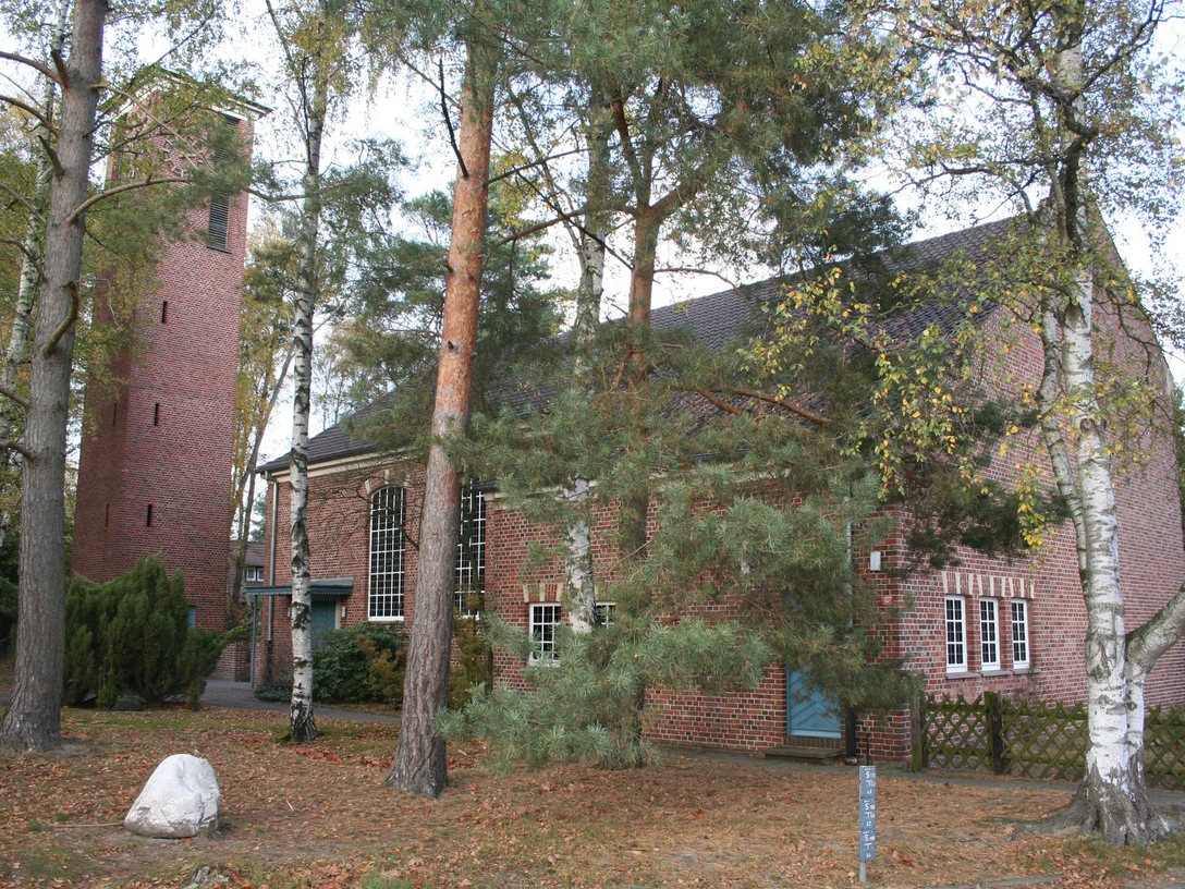 St. Johannis Kirche Backstein-Kirche im Grünen mit Turm und Fenstern; Bäume im Vordergrund lassen Licht schimmern.