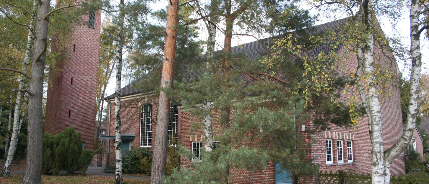 St. Johannis Kirche Backstein-Kirche im Grünen mit Turm und Fenstern; Bäume im Vordergrund lassen Licht schimmern.