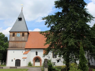 St. Katharinen Kirchen Weißgetünchte Kirche mit rotem Dach und hohem Uhrturm, umgeben von Bäumen unter einem blauen Himmel.