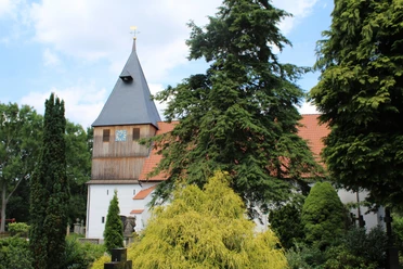 Kirche Steyerberg-Rießen Kirche in Steyerberg-Rießen mit markantem Turm, umgeben von hohen Bäumen und bunten Sträuchern.