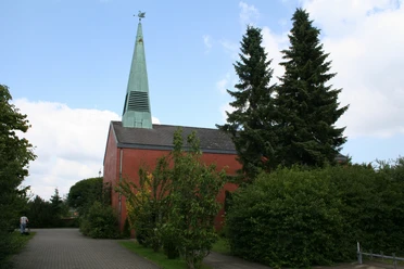 St. Lebuin Kapelle Roter Backsteinbau mit grünem Kirchturm und angrenzenden Bäumen bei bewölktem Himmel.