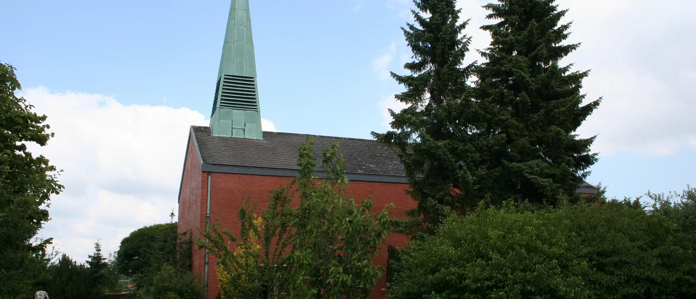 St. Lebuin Kapelle Roter Backsteinbau mit grünem Kirchturm und angrenzenden Bäumen bei bewölktem Himmel.