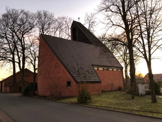 Eine moderne Backsteinkirche mit steilem Dach, umgeben von Bäumen, aufgenommen in der Dämmerung.
