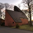 Eine moderne Backsteinkirche mit steilem Dach, umgeben von Bäumen, aufgenommen in der Dämmerung.