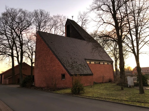 A modern brick church with a steep roof, surrounded by trees, photographed at dusk.