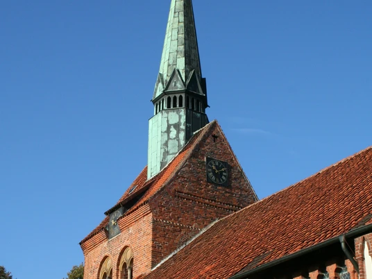 Backsteinkirche in Heemsen mit markantem, grün oxidiertem Kupferturm und Uhr vor klarem Himmel.