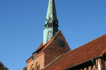 St. Michaelis-Kirche Heemsen Backsteinkirche in Heemsen mit markantem, grün oxidiertem Kupferturm und Uhr vor klarem Himmel.