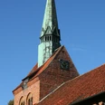 St. Michaelis-Kirche Heemsen Backsteinkirche in Heemsen mit markantem, grün oxidiertem Kupferturm und Uhr vor klarem Himmel.