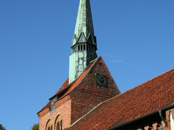 St. Michaelis-Kirche Heemsen Backsteinkirche in Heemsen mit markantem, grün oxidiertem Kupferturm und Uhr vor klarem Himmel.