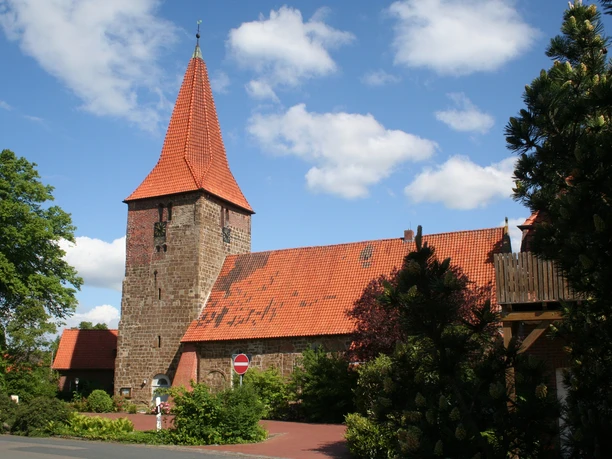 St.-Bartholomäus-Kirche in Balge St.-Bartholomäus-Kirche in Balge mit markantem rotem Backstein und spitzem Turm, umgeben von Bäumen.
