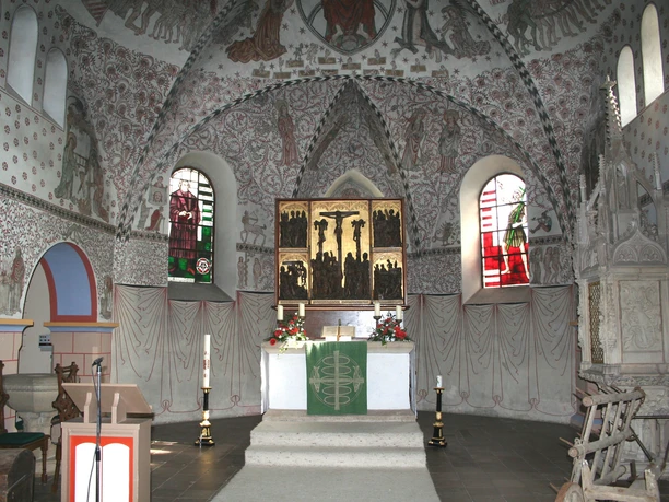 Romanische Kirche mit prächtigen, farbenfrohen Wandmalereien und einem kunstvollen Altarraum.