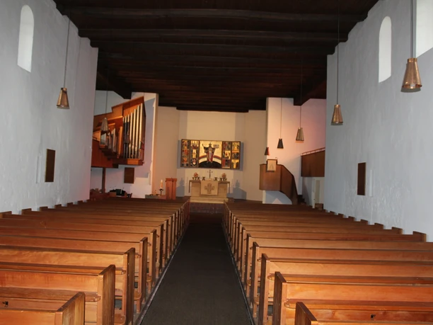 Innenansicht der St.-Gangolf-Kirche Wietzen mit Holzbänken und einem Altar im Mittelpunkt des Raumes.