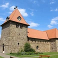 Rundturm-Kirche aus Naturstein mit rotem Ziegeldach, umgeben von parkähnlicher Grünanlage.