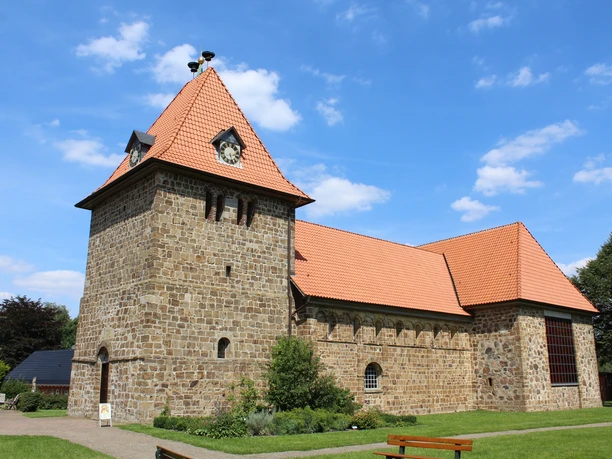 St.-Gangolf-Kirche in Wietzen Rundturm-Kirche aus Naturstein mit rotem Ziegeldach, umgeben von parkähnlicher Grünanlage.