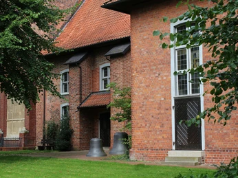 St.-Marcellus-Kirche Asendorf Backsteinkirche mit roten Dachziegeln, umgeben von Grün, Kirchturmglocken am Eingang platziert.