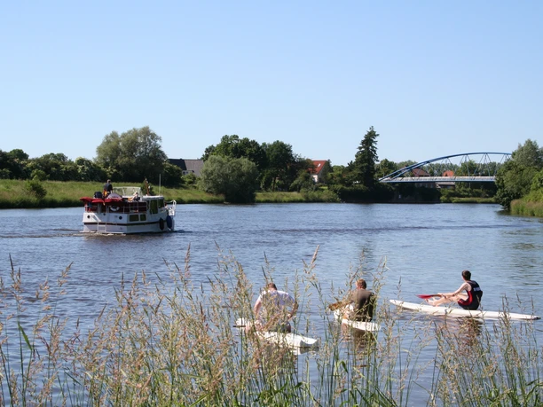Standup Paddling Drei Personen beim Standup Paddling auf einem Fluss, im Hintergrund ein vorbeifahrendes Boot.