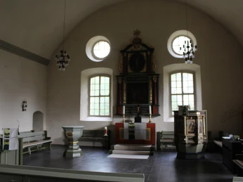 Kircheninnenraum mit Kanzel, Taufbecken und Altar; helle Wände, gewölbte Decke und große Fenster.