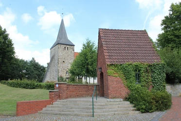 St. Dionysius-Kirche in Steimbke mit historischer Architektur, neben einem kleinen, efeubewachsenen Gebäude.