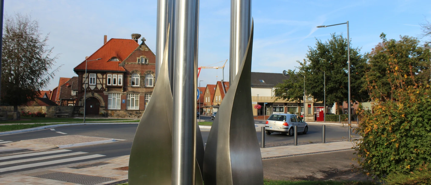 Drei hohe, spiralförmige Metallsäulen stehen in einem städtischen Umfeld mit traditionellen Gebäuden.