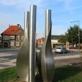Skulptur Stundenrot schenkt nichts als Blätter Drei hohe, spiralförmige Metallsäulen stehen in einem städtischen Umfeld mit traditionellen Gebäuden.