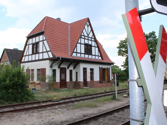 Ein historisches Fachwerkgebäude steht neben Gleisen unter einem wolkigen Himmel am Südbahnhof Weyhe.