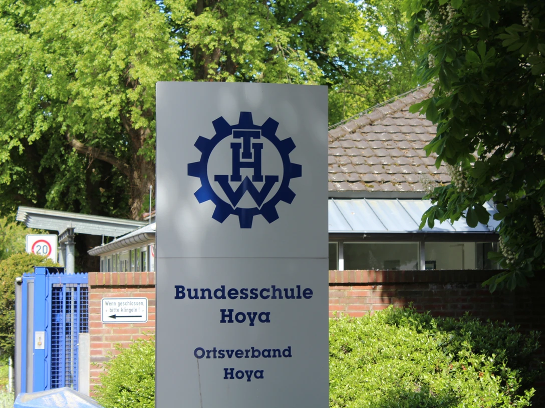 THW Hoya Schild der THW Bundesschule Hoya mit Logo, vor einem Ziegelgebäude und grüner Vegetation.