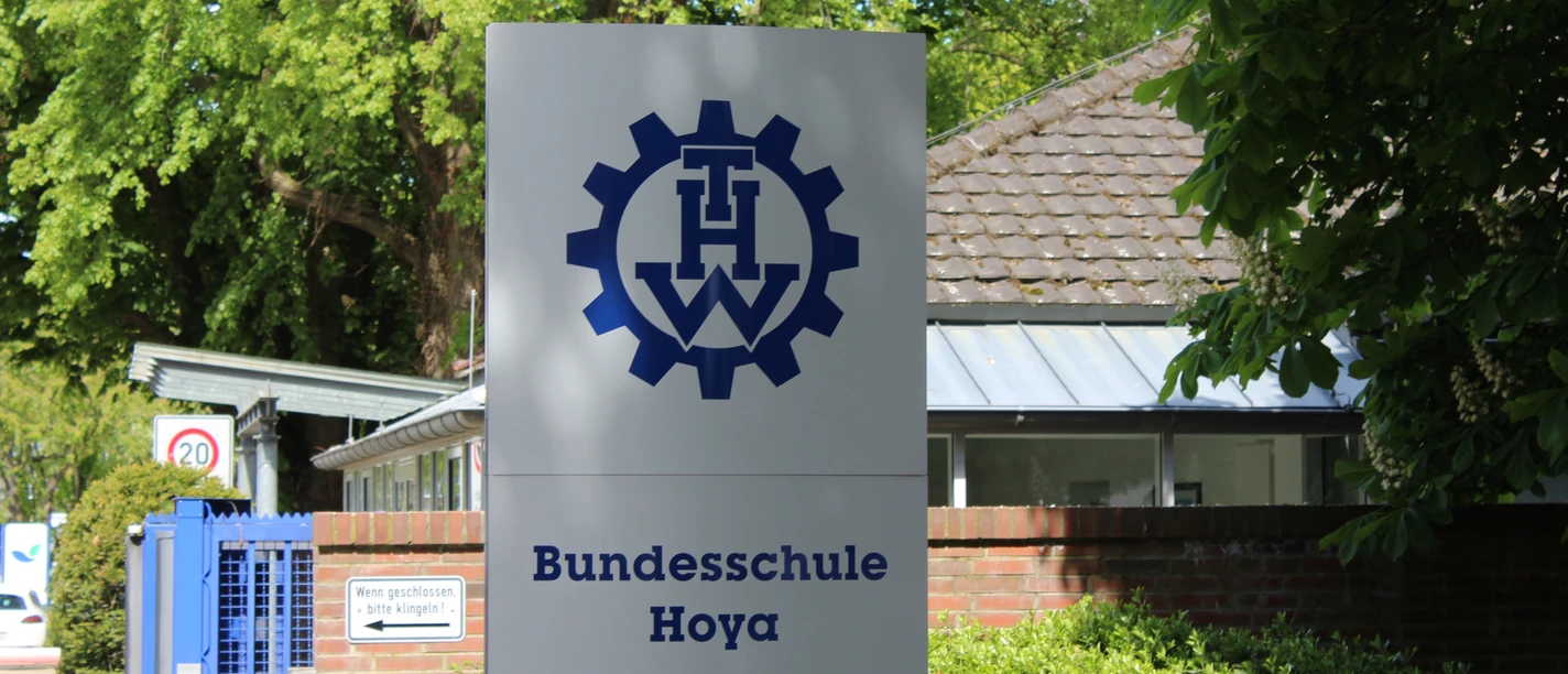 THW Hoya Schild der THW Bundesschule Hoya mit Logo, vor einem Ziegelgebäude und grüner Vegetation.