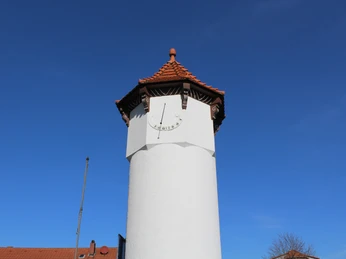 Uhrturm in Rehburg-Loccum mit giebelrotem Ziegeldach vor strahlend blauem Himmel.