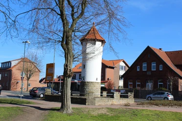 Der historische Uhrturm von Rehburg-Loccum mit rotem Ziegeldach, umgeben von Bäumen und Wohnhäusern.